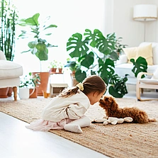 Illustration - Ihr Experte für schönes Wohnen - Kleines Mädchen, das mit Hund spielt, im Wohnzimmer auf einem Naturfaserteppich.