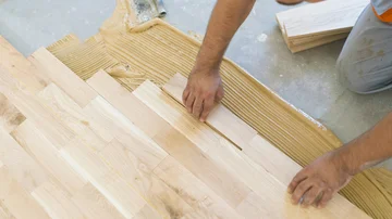 Handwerker verlegt und verklebt Parkett, Muster Schiffsboden oder gerader Verband